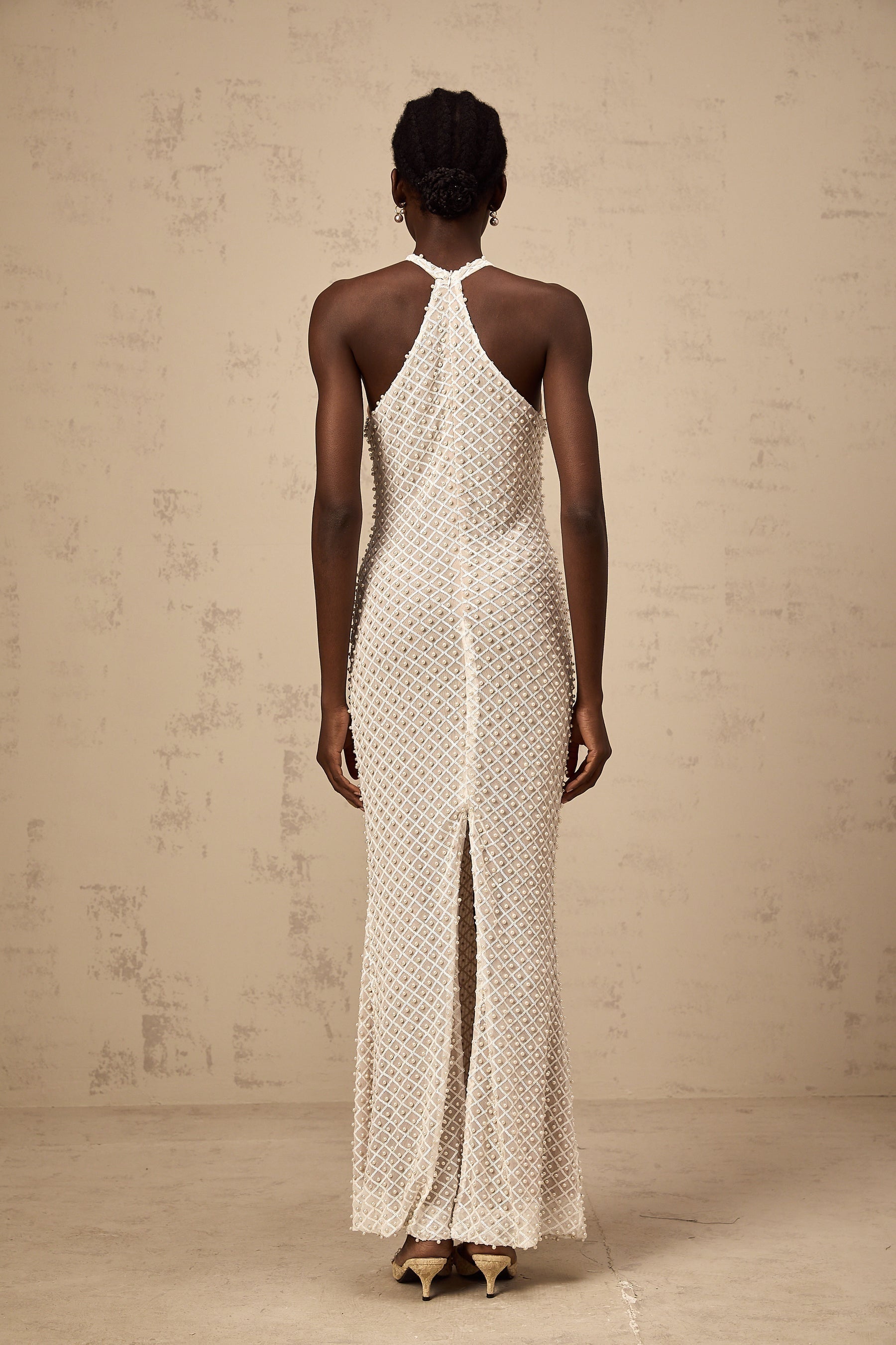 Woman wearing long white halterneck maxi dress with embellished details standing against plain background