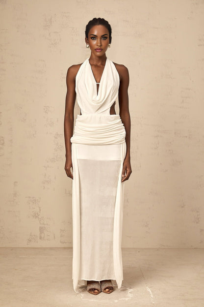 Woman wearing long white halterneck maxi dress with open back standing against plain background