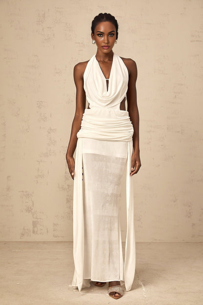 Woman wearing long white halterneck maxi dress with open back standing in front of plain background