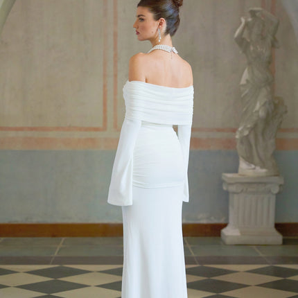 Woman wearing long white knit dress with glittery floral appliques standing against plain background