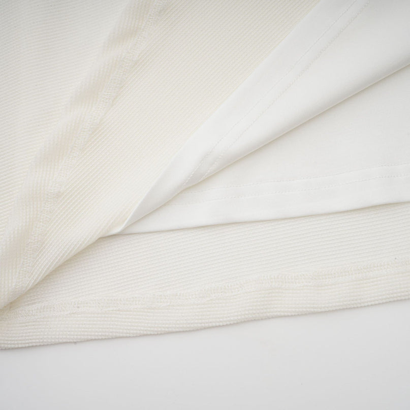 Woman wearing long white knit maxi dress with glittery floral appliques standing in front of plain background