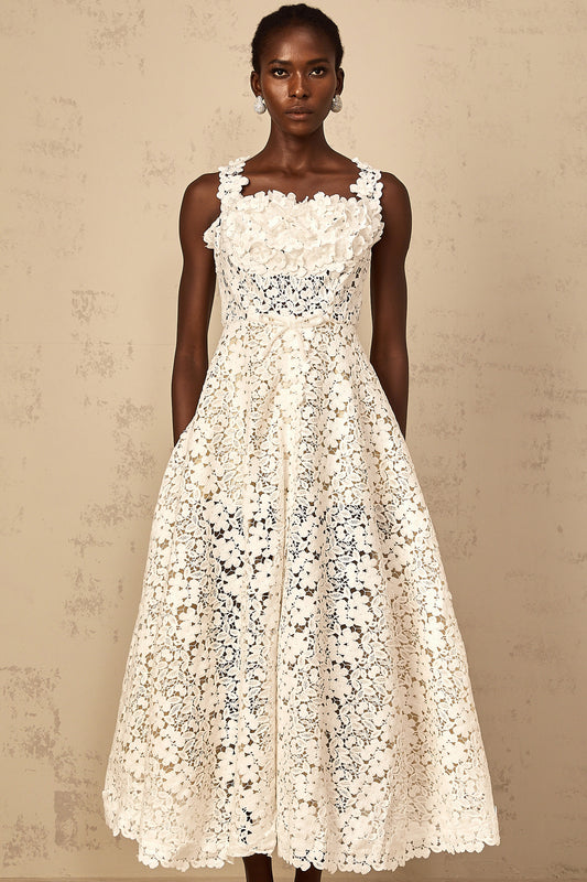 Woman wearing long white lace maxi dress with shirred detailing and corded lace pattern standing against plain background