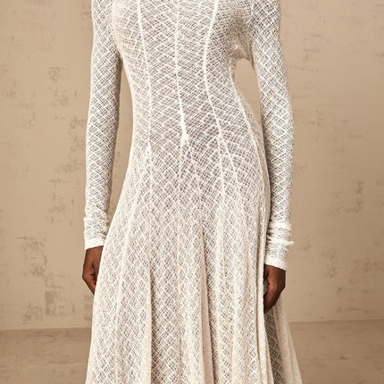 Woman wearing long white lace maxi dress with wavy pattern and sleeveless design standing against plain background