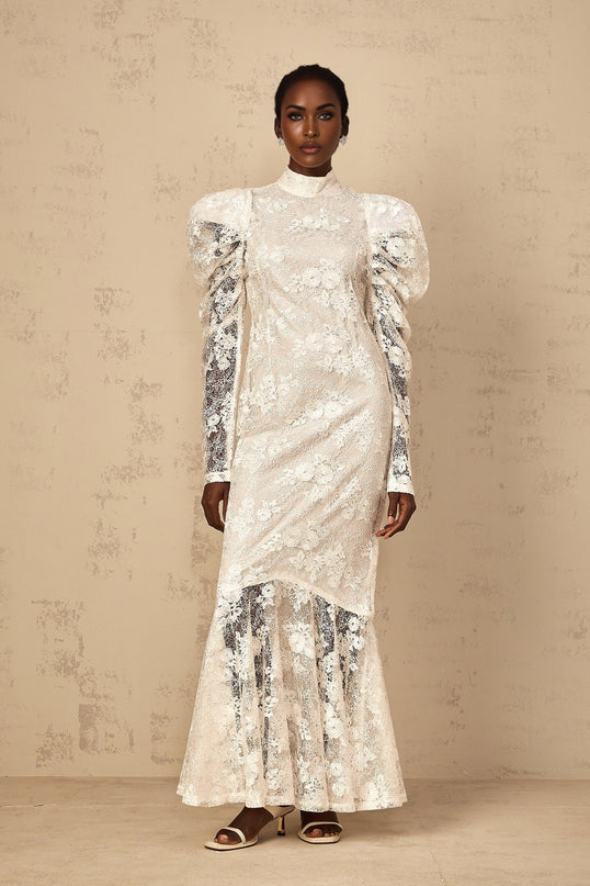 Woman wearing long white lace mermaid style dress with floral pattern and fitted silhouette