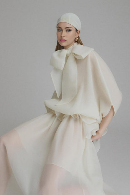 Woman wearing long white maxi dress with tie neck and ruffled details standing in relaxed pose