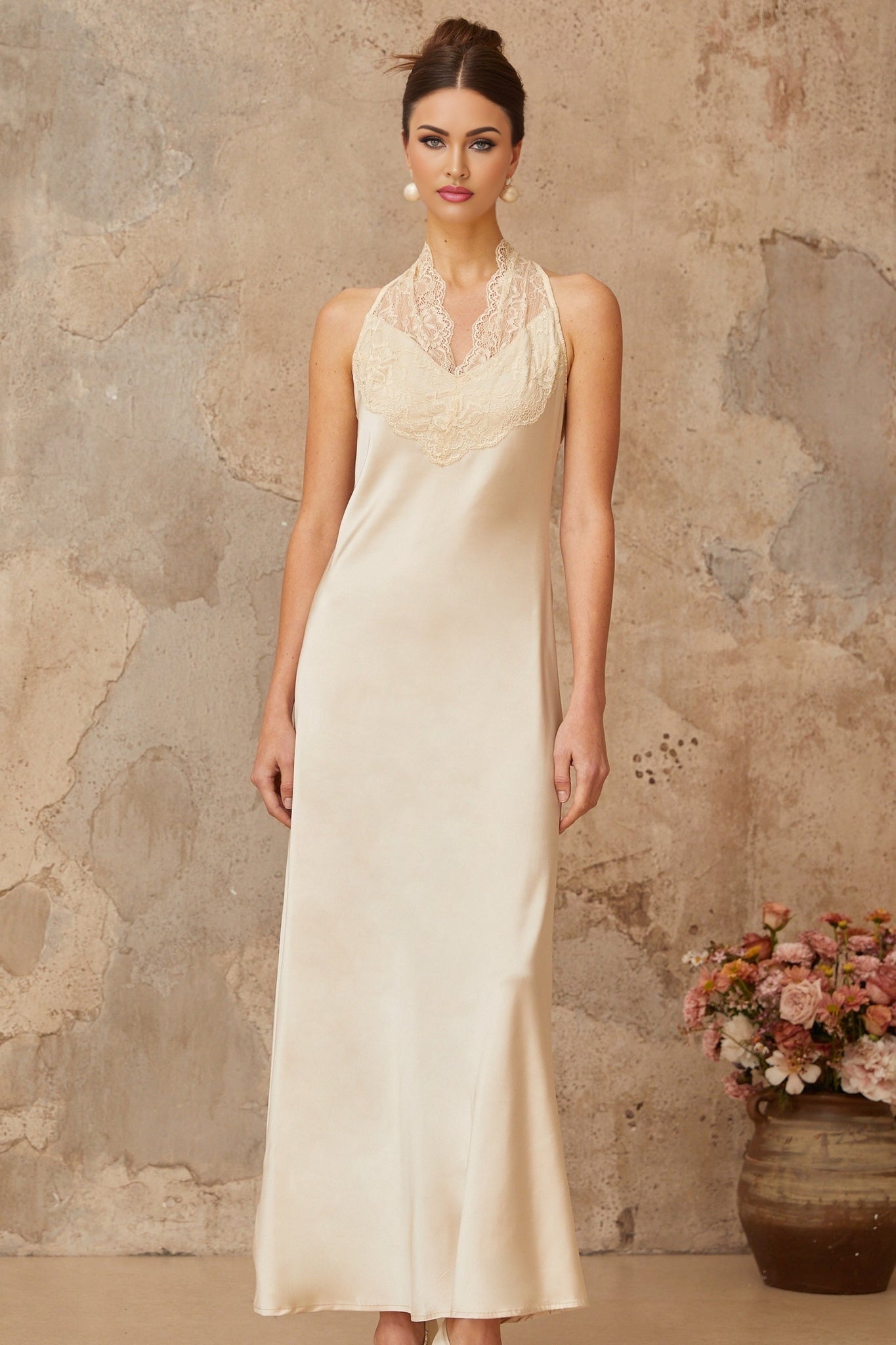 Woman wearing long white satin maxi dress with lace trim details standing against plain background