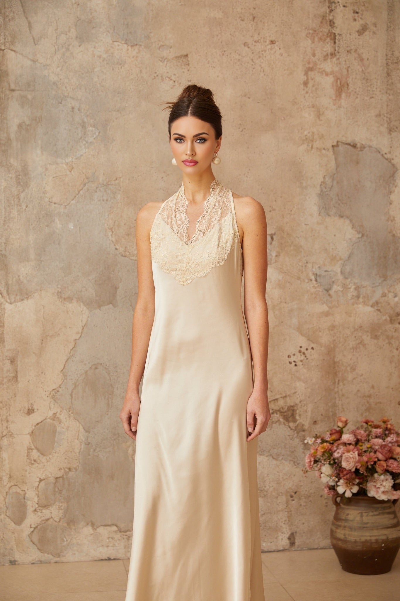 Woman wearing long white satin maxi dress with lace trim details standing in elegant pose