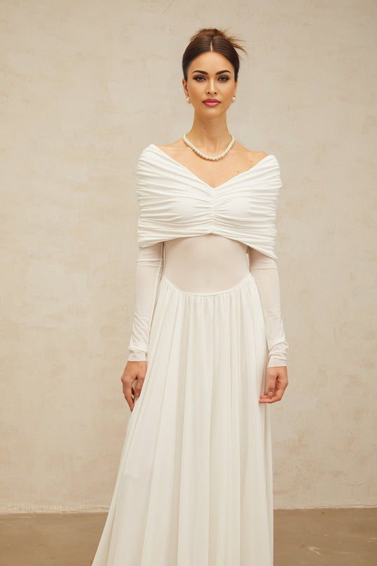 Woman wearing long white sleeveless maxi dress with draped details and ruched fabric standing against plain background