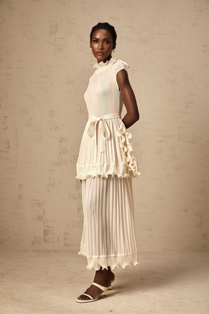 Woman wearing long white sleeveless maxi dress with ruffle details and pleated skirt