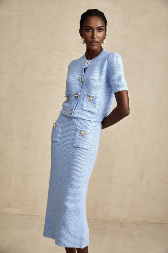 Woman wearing matching blue knit blouse and skirt set standing against plain background