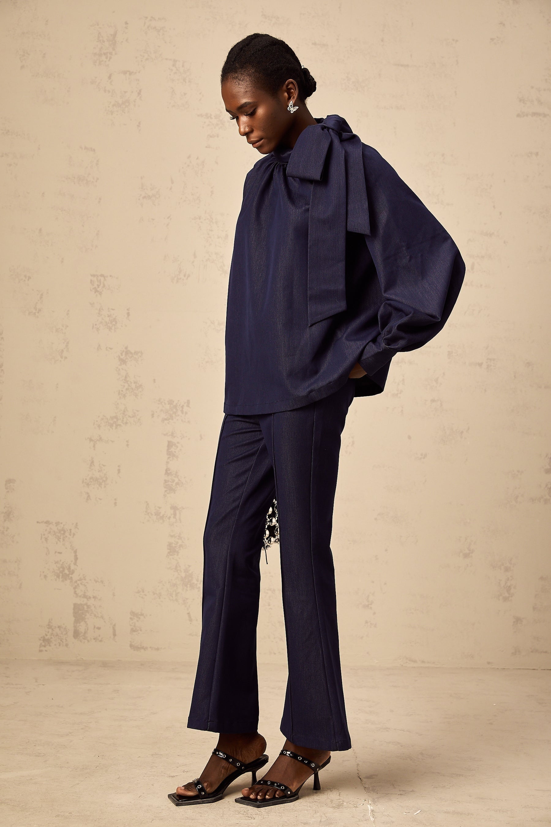 Woman wearing matching denim blue blouse and trousers set Blouse has flared sleeves Trousers are wide leg style Outfit has retro inspired look