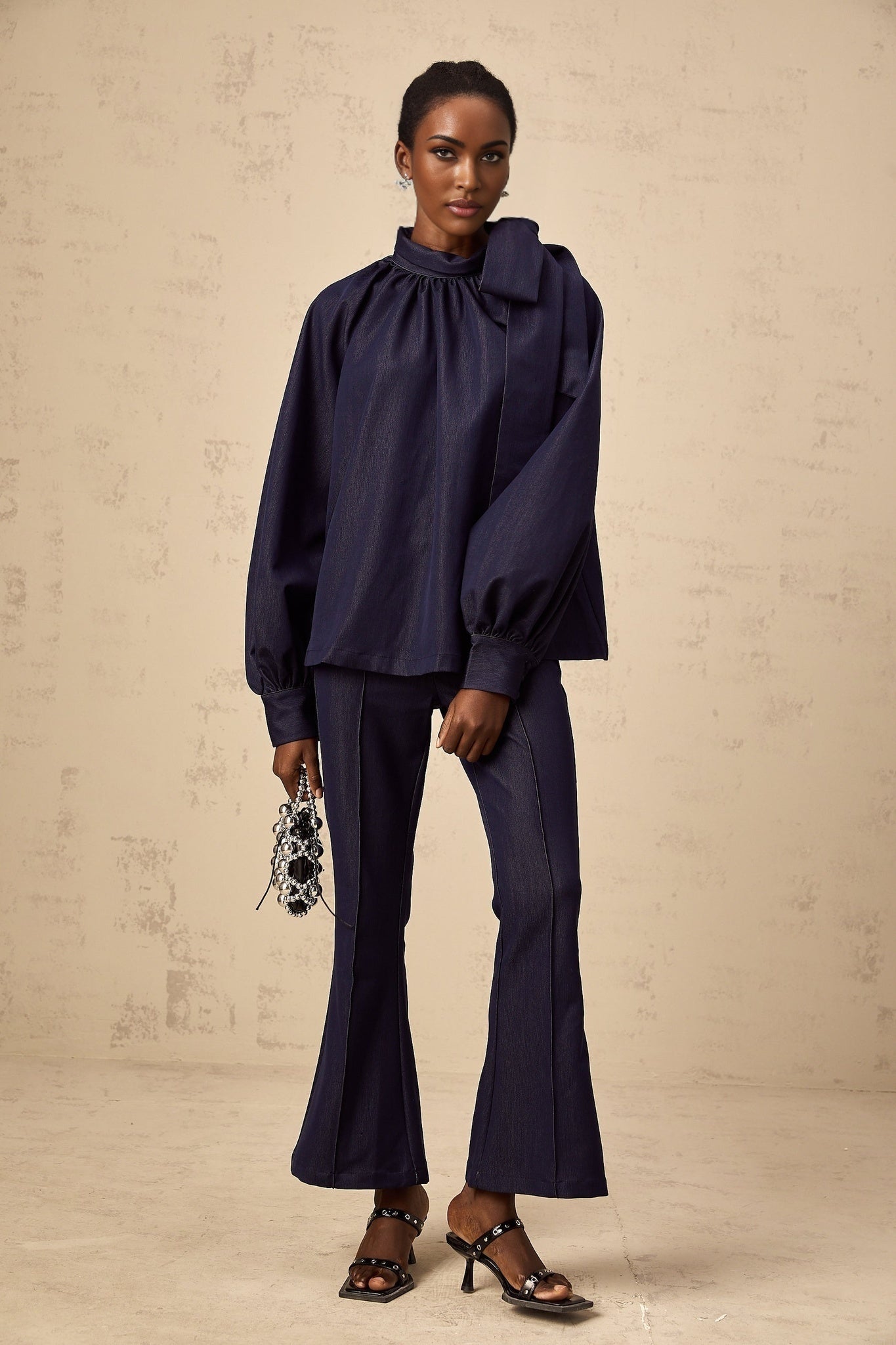 Woman wearing matching denim blue blouse and trousers set Blouse has flared sleeves Trousers are wide leg style Set named Mathilde