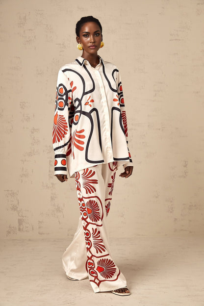 Woman wearing matching floral print shirt and trousers set in vibrant colors standing against plain background