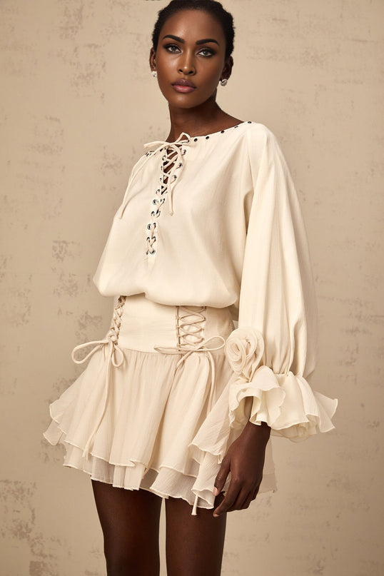 Woman wearing matching white blouse and skirt set blouse has ruffled details and self tie bow at neckline skirt falls to midi length