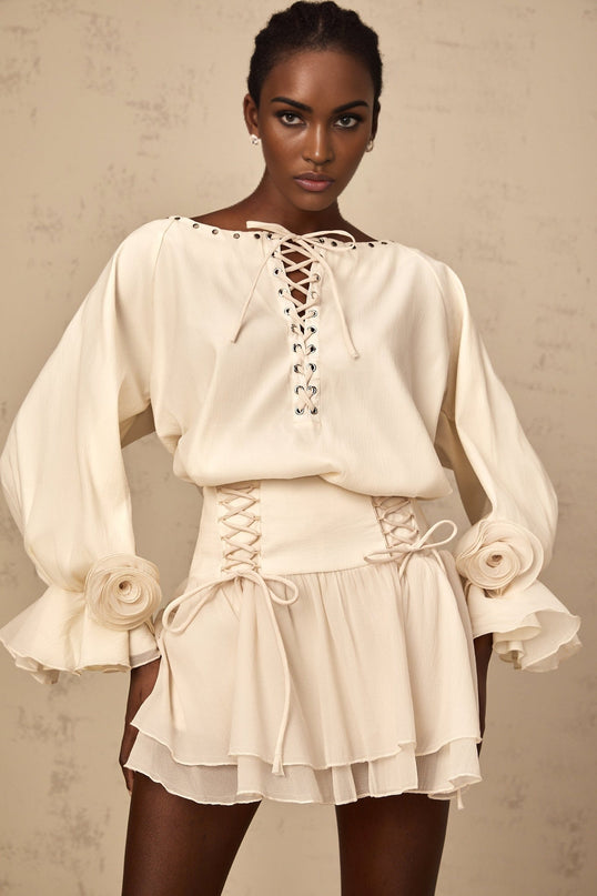 Woman wearing matching white blouse and skirt set with ruffles and self tie detail