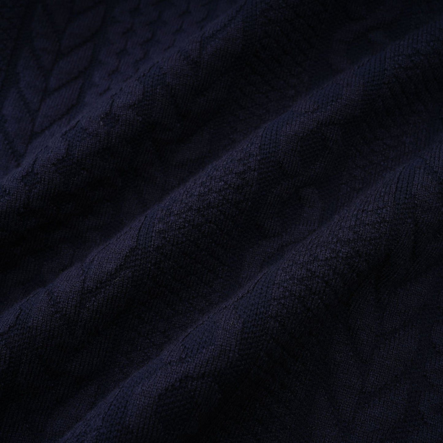 Woman wearing navy blue crochet knit cardigan and matching trousers standing against plain background