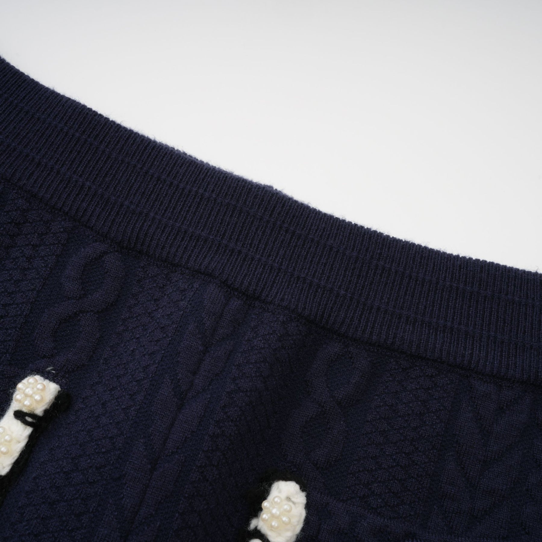 Woman wearing navy blue crochet knit cardigan and matching trousers standing against plain background