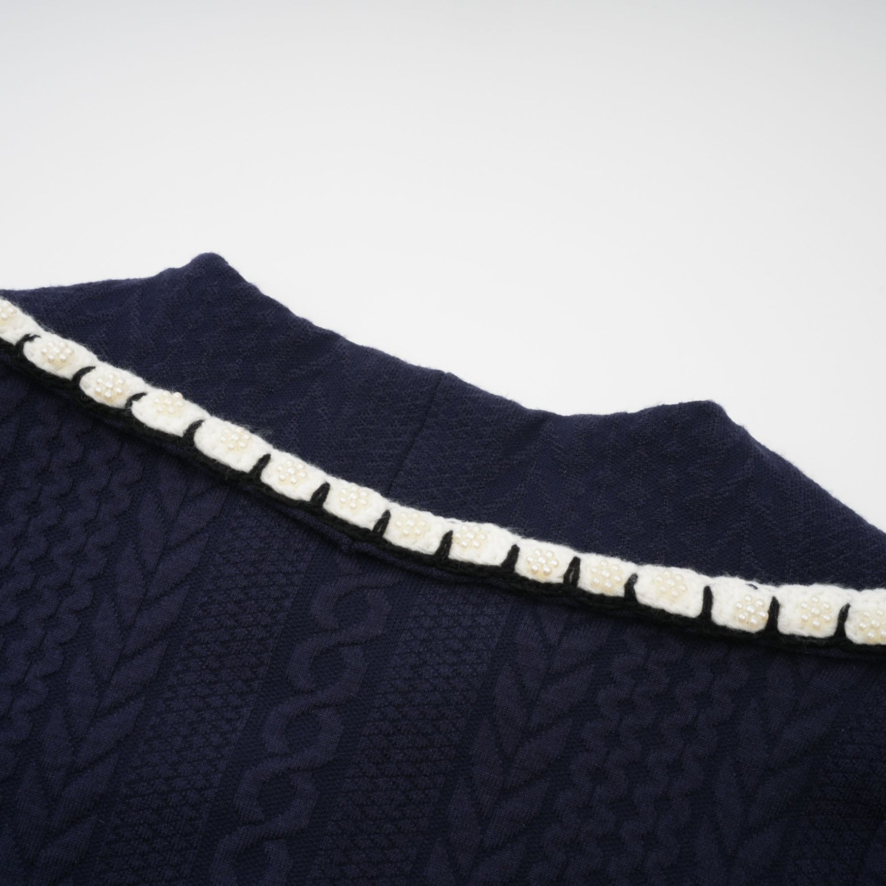 Woman wearing navy blue crochet knit cardigan and matching trousers standing against plain background