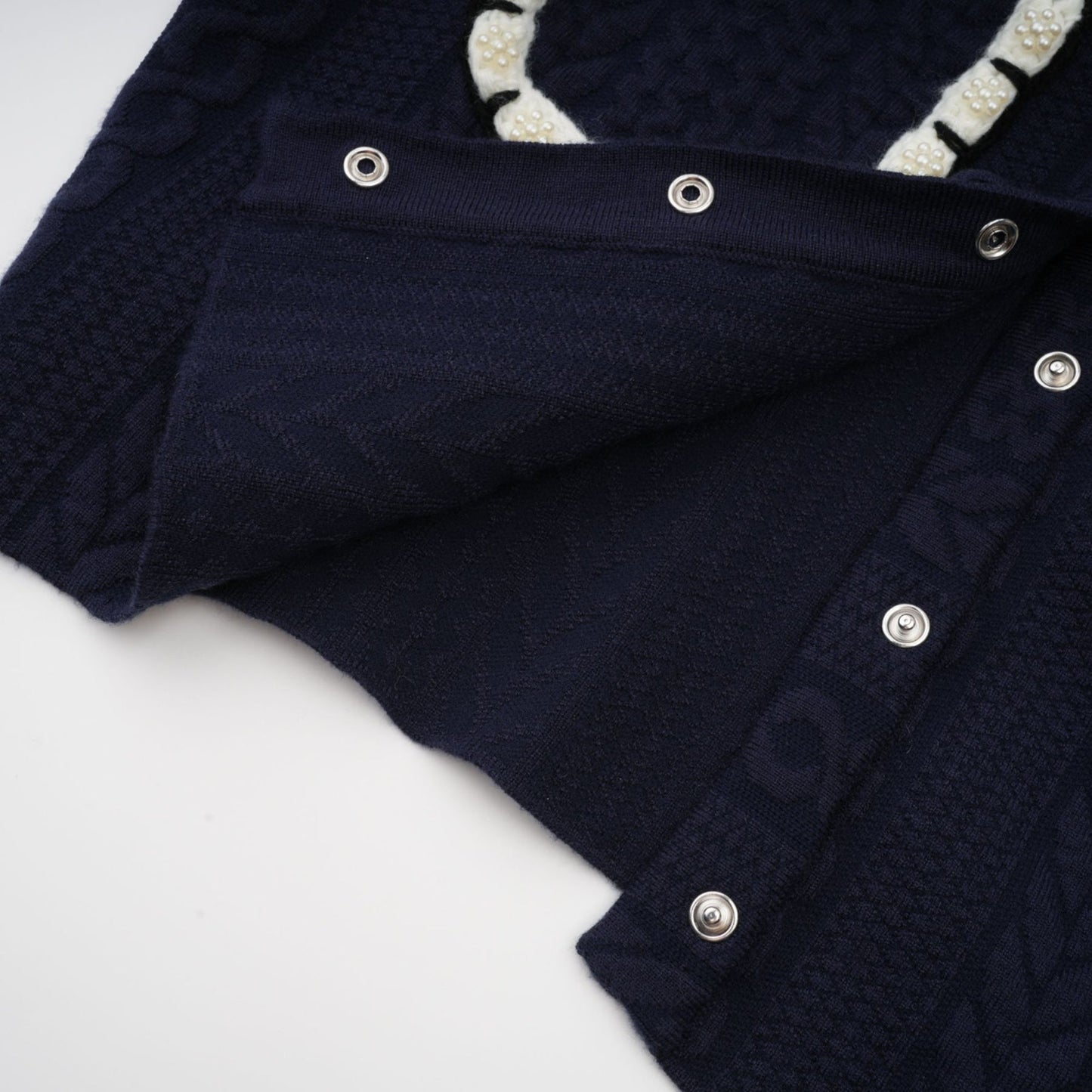 Woman wearing navy blue crochet knit cardigan and matching trousers standing against plain background