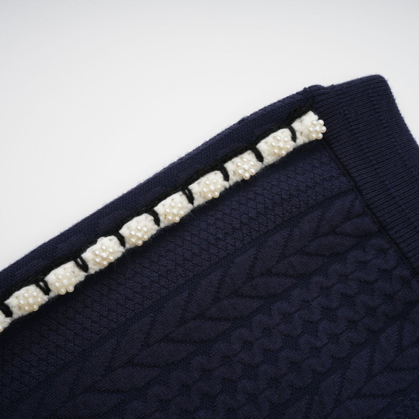 Woman wearing navy blue crochet knit cardigan and matching trousers standing against plain background