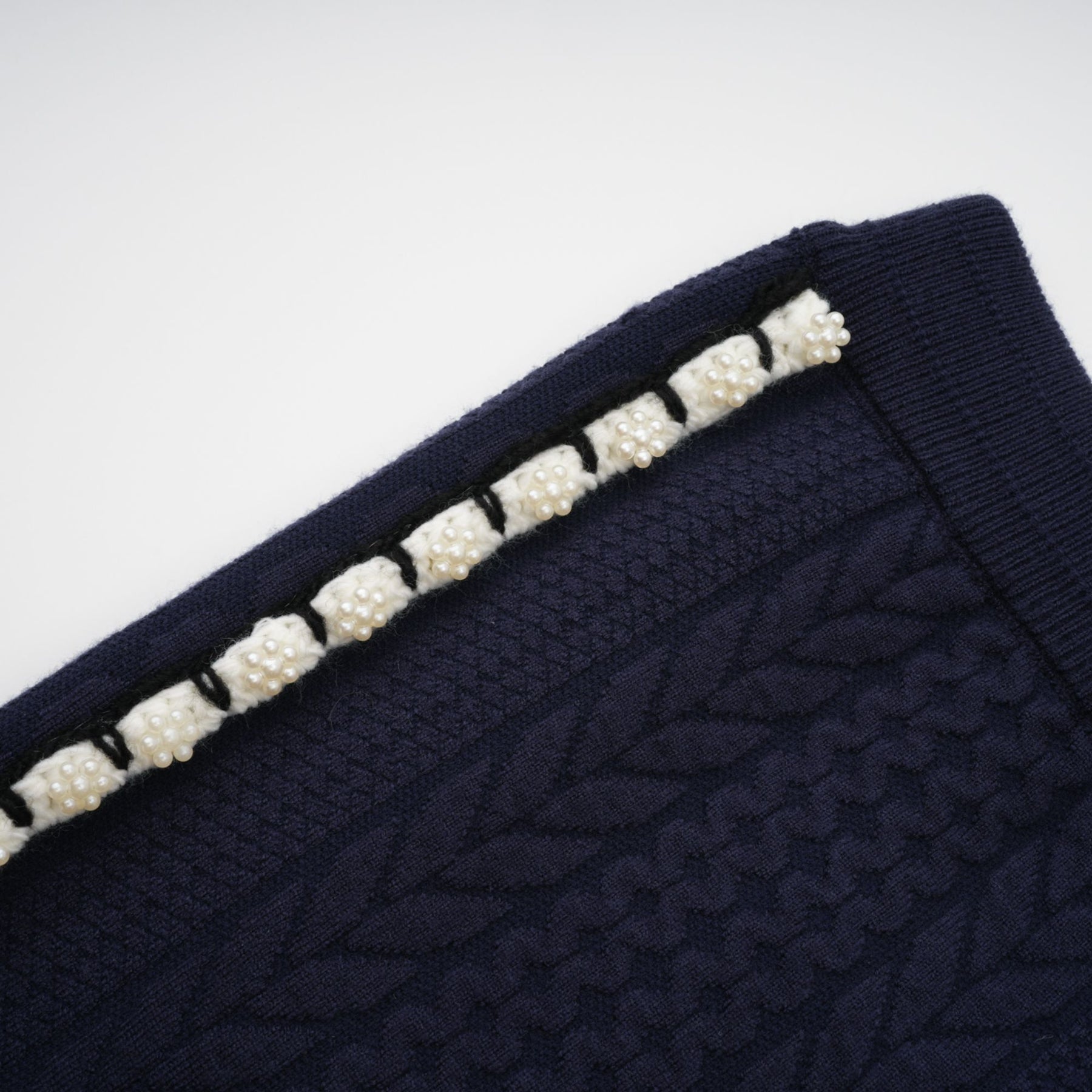 Woman wearing navy blue crochet knit cardigan and matching trousers standing against plain background
