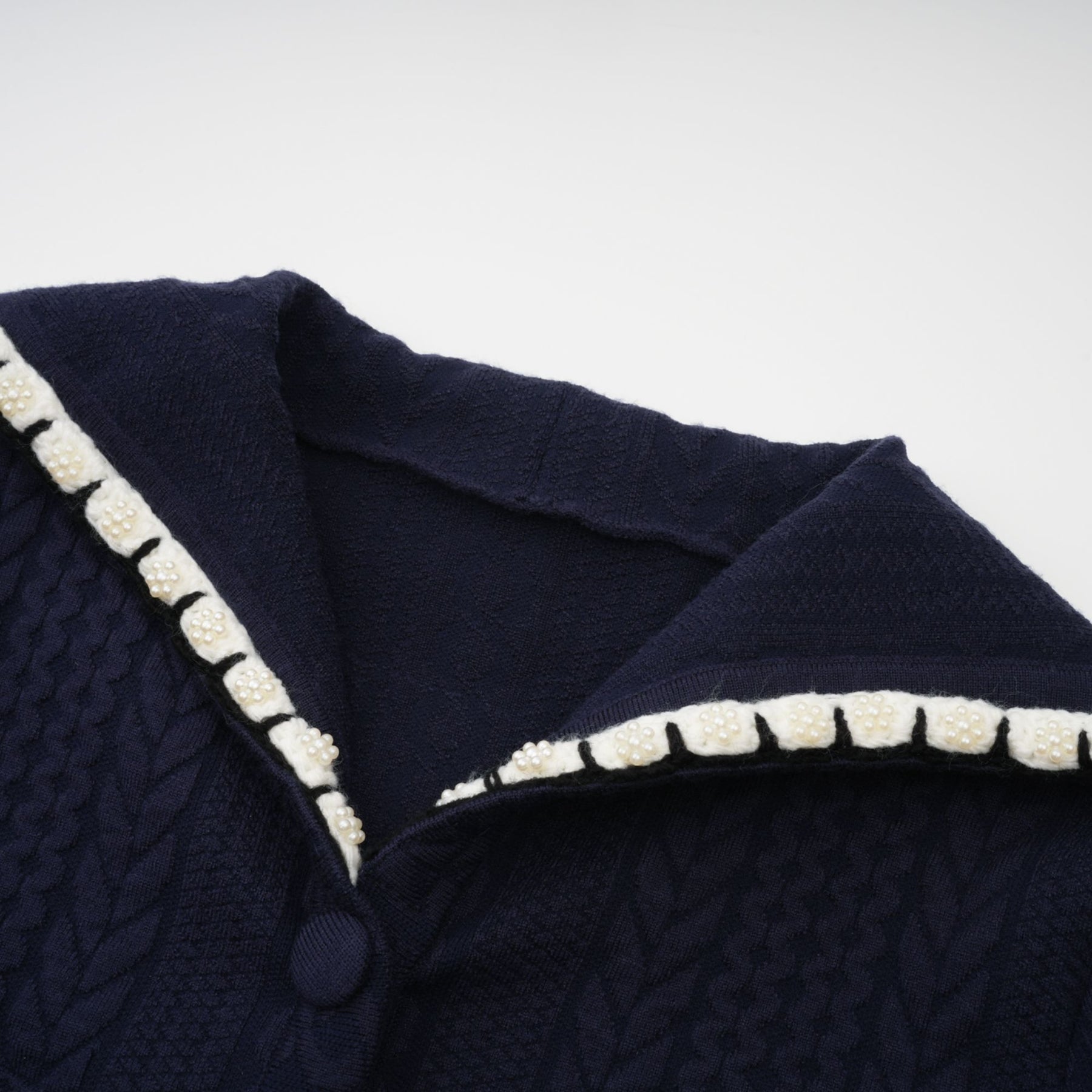 Woman wearing navy blue crochet knit cardigan and matching trousers standing against plain background