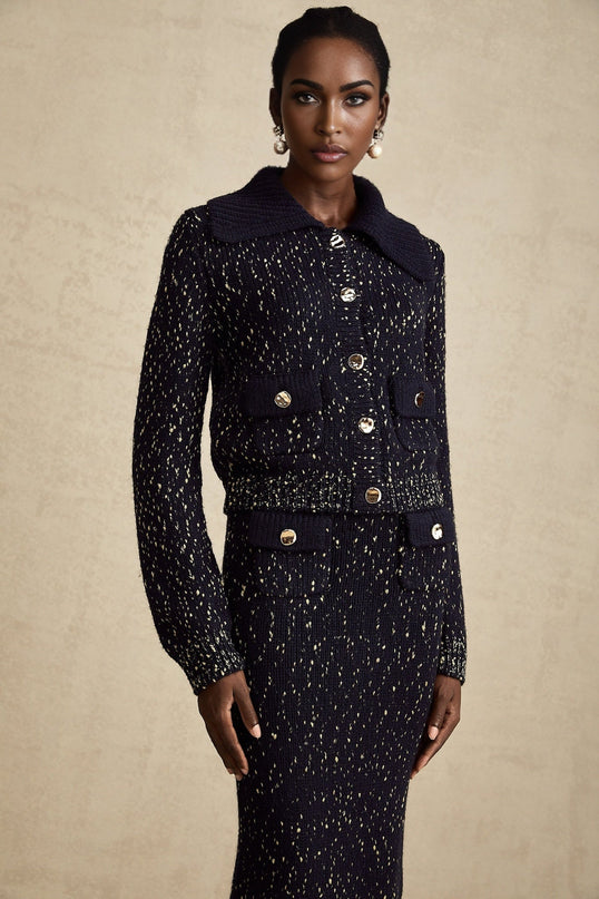 Woman wearing navy blue crochet knit jacket and matching skirt set standing against plain background