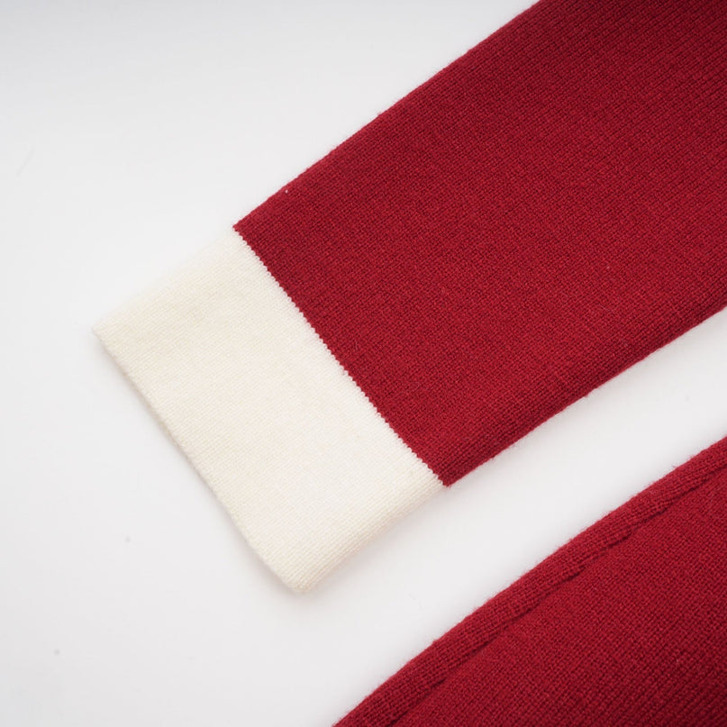 Woman wearing navy blue offshoulder knit midi dress with fitted silhouette and long sleeves standing against plain background