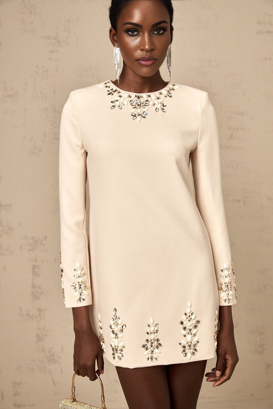 Woman wearing neutral colored long sleeved mini dress adorned with crystal embellishments
