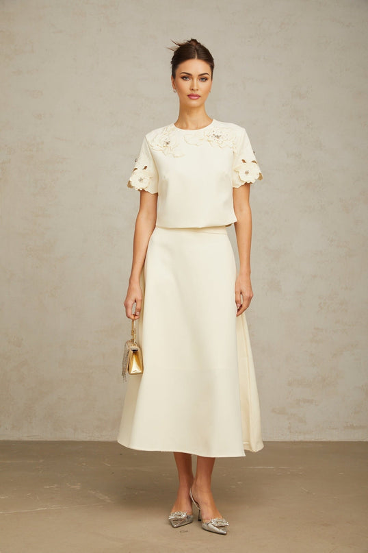 Woman wearing neutral colored matching set with three dimensional petal details on top and skirt