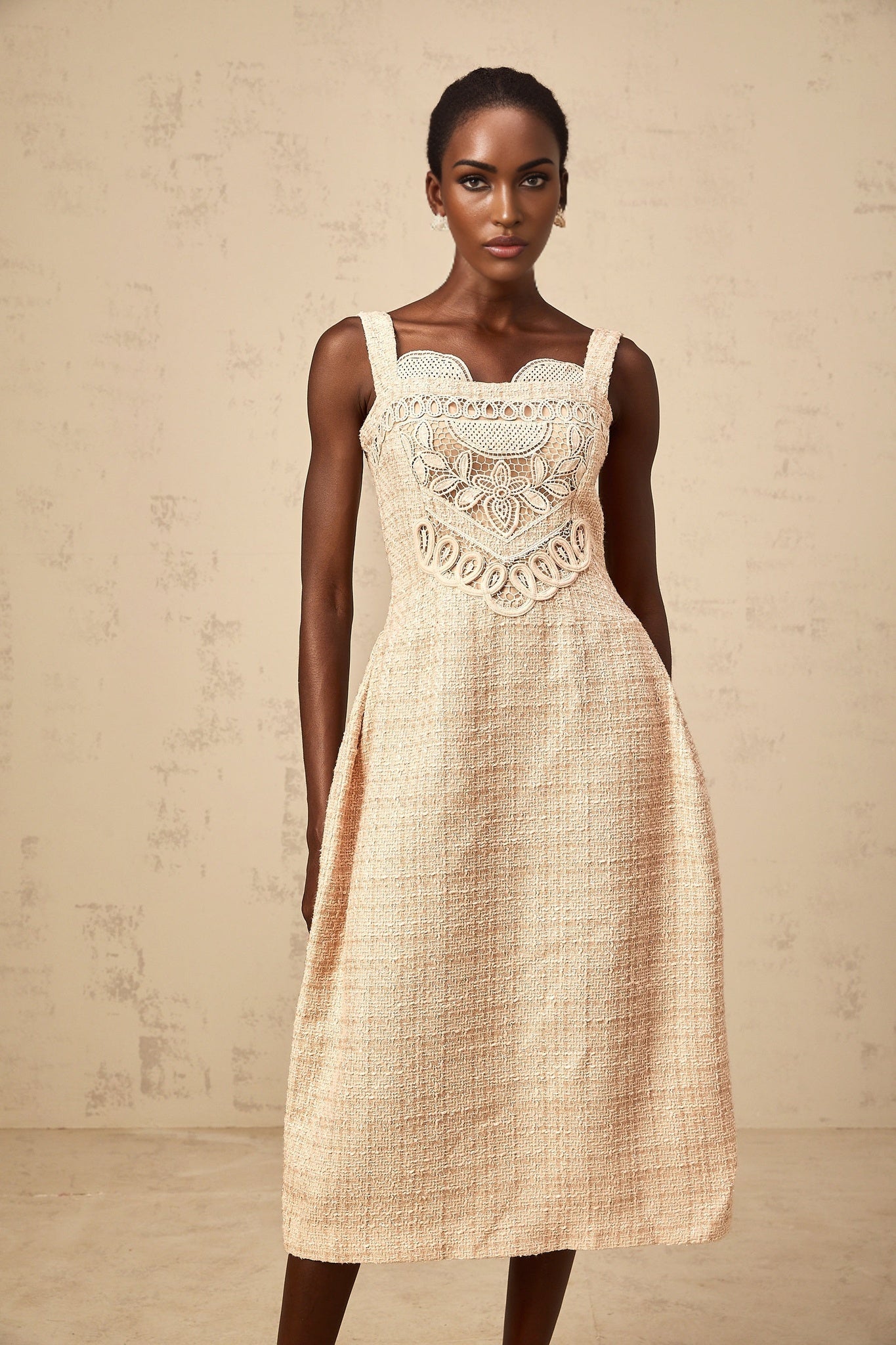 Woman wearing neutral colored mini dress with interwoven embroidery pattern standing against plain background