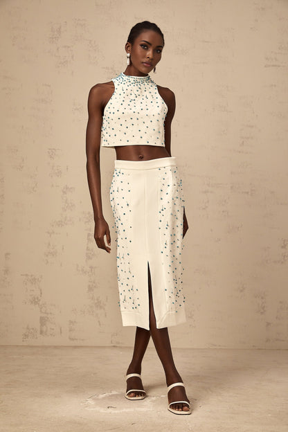 Woman wearing off white two piece outfit consisting of embellished top and matching skirt