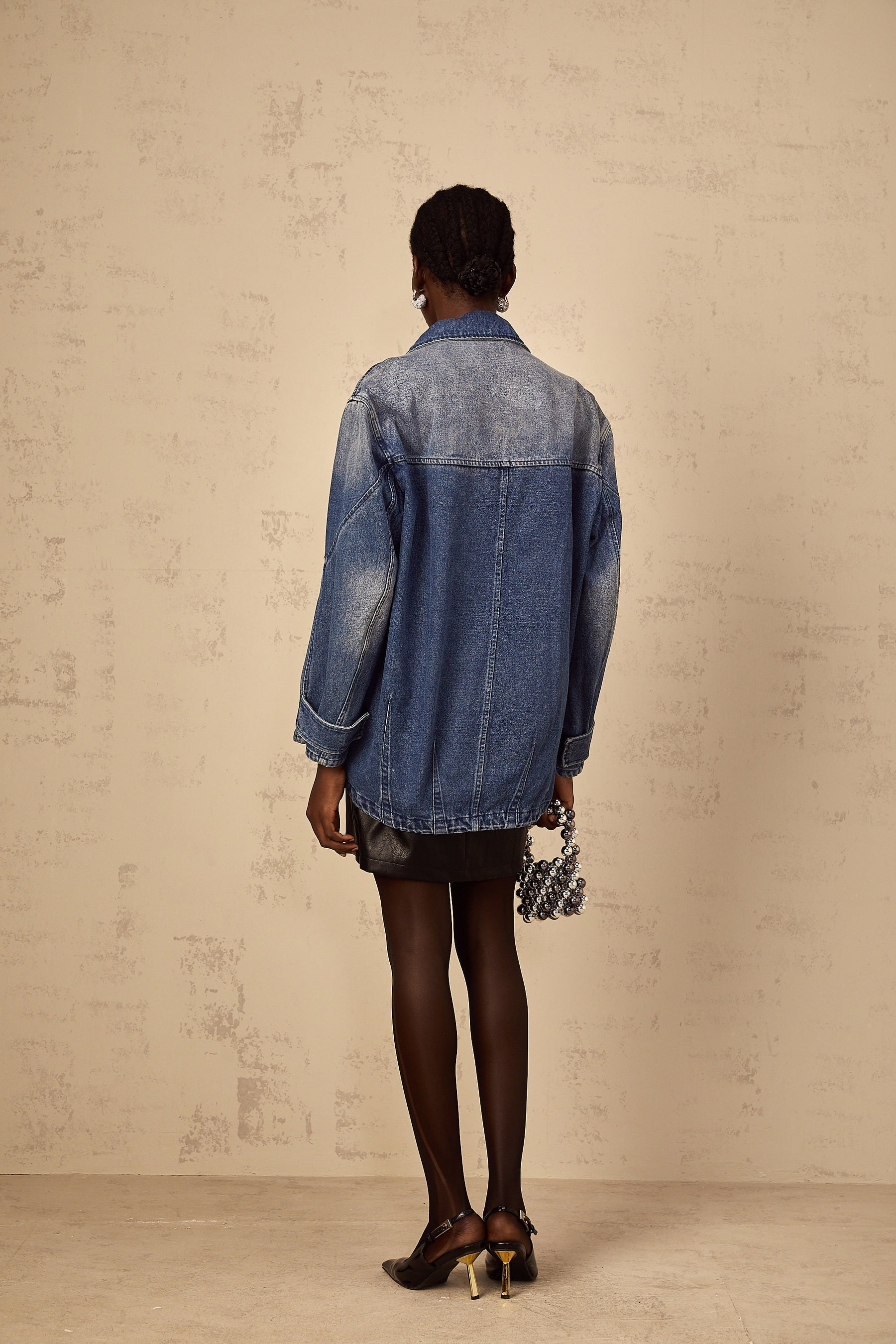 Woman wearing oversized blue denim jacket with patchwork design and loose fit