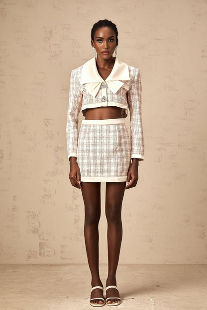 Woman wearing pink checked tweed jacket and matching skirt set standing against plain background