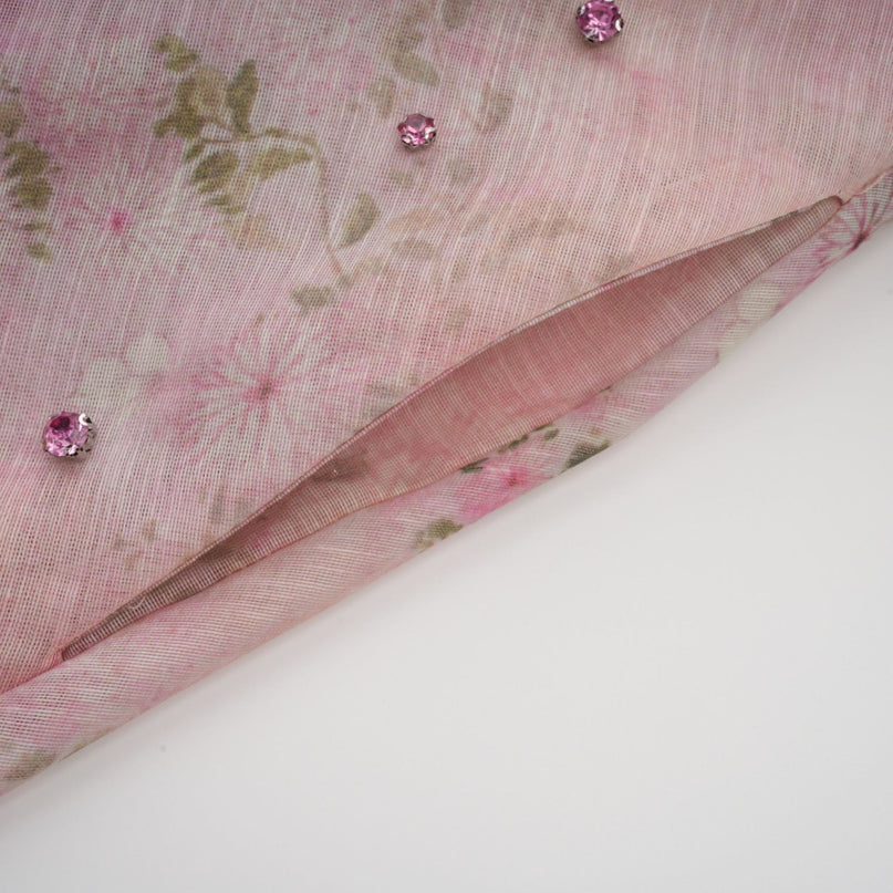 Woman wearing pink floral print midi dress with embellishments standing in elegant pose against plain background