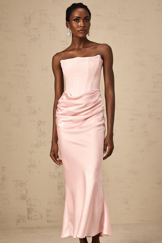 Woman wearing pink offshoulder maxi dress with flowing skirt standing in sunlit garden