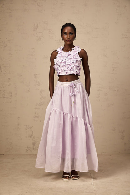 Woman wearing purple two piece outfit consisting of floral top and matching skirt with faux flower design