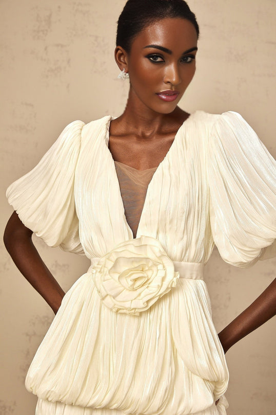 Woman wearing short beige dress with pleated skirt and floral applique details