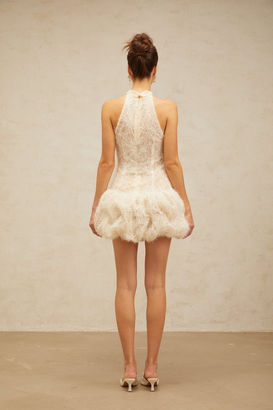 Woman wearing short beige mini dress with puff sleeves and textured fabric