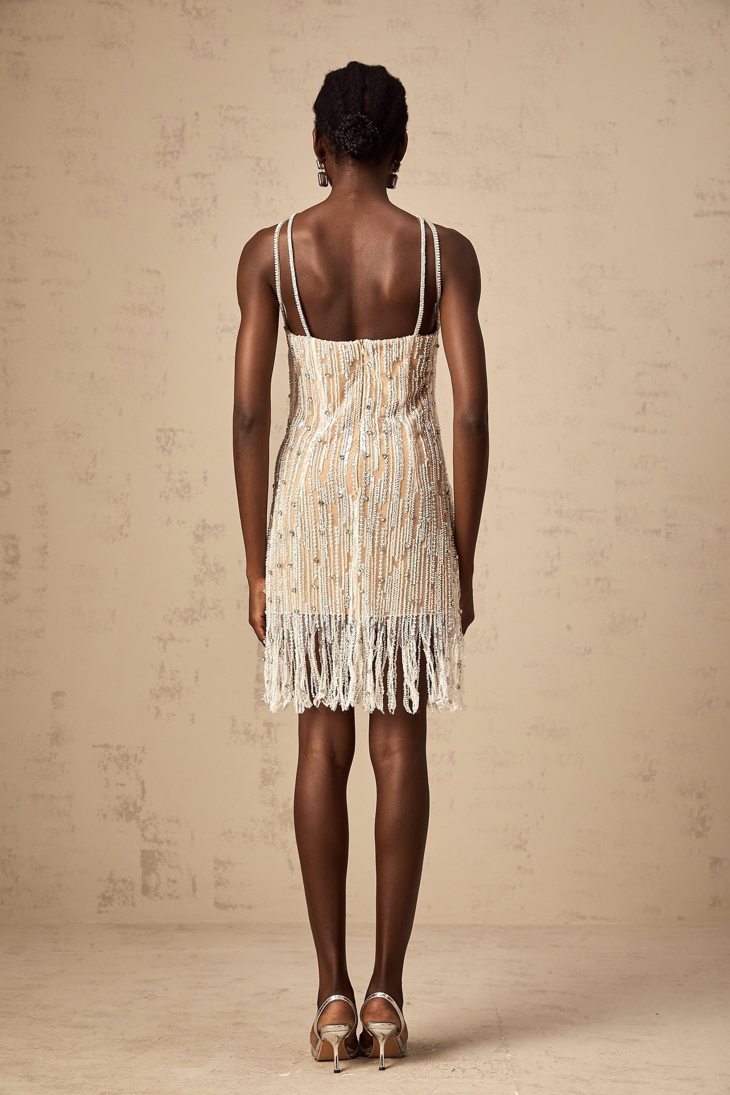 Woman wearing short black dress with sparkly embellishments and fringe details at hem