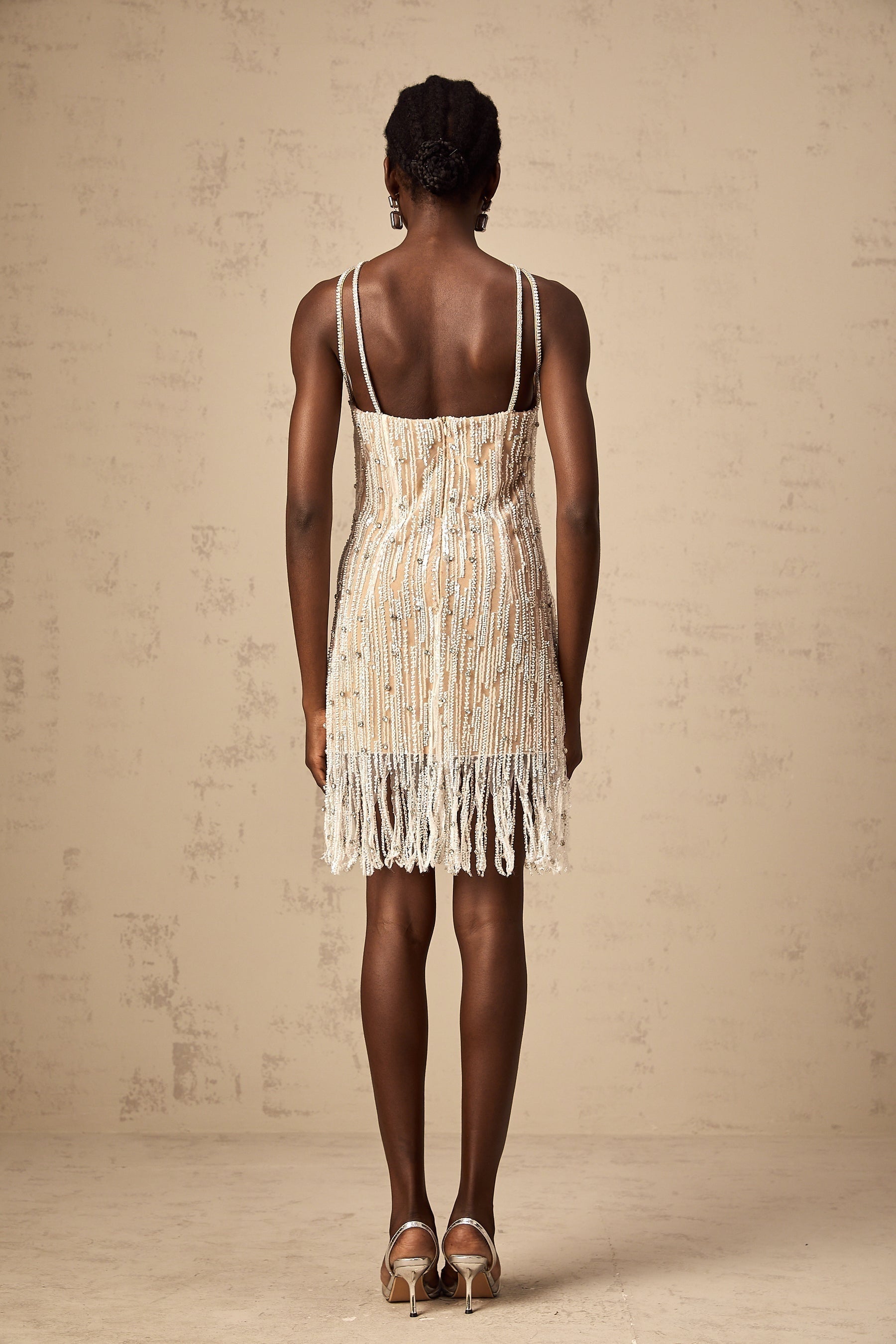 Woman wearing short black dress with sparkly embellishments and fringe details at hem