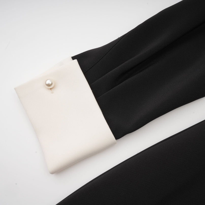 Woman wearing short black mini dress with white contrast collar and cuffs featuring crystal embellishments