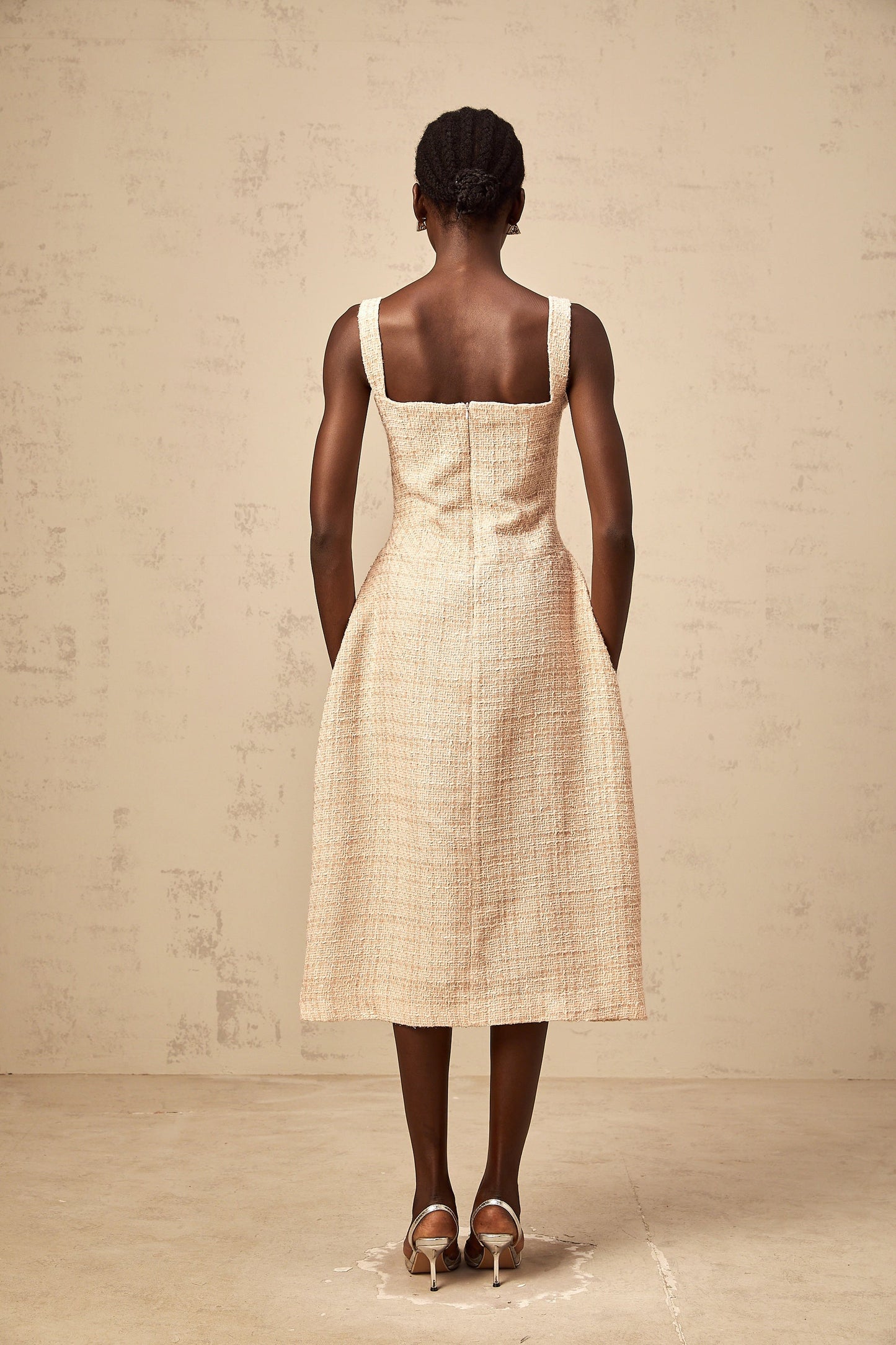 Woman wearing short neutral colored dress with intricate embroidery pattern standing against plain background