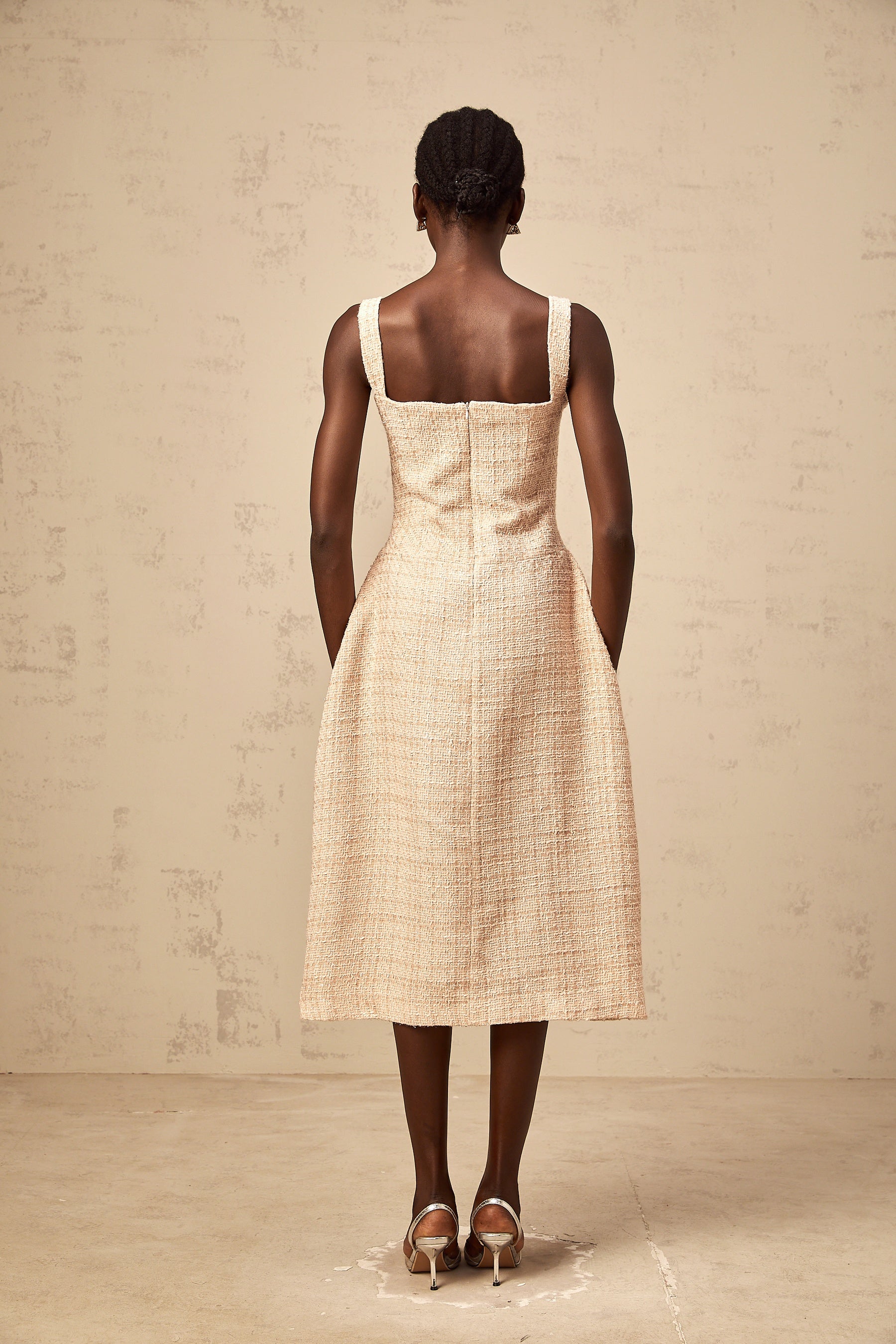 Woman wearing short neutral colored dress with intricate embroidery pattern standing against plain background