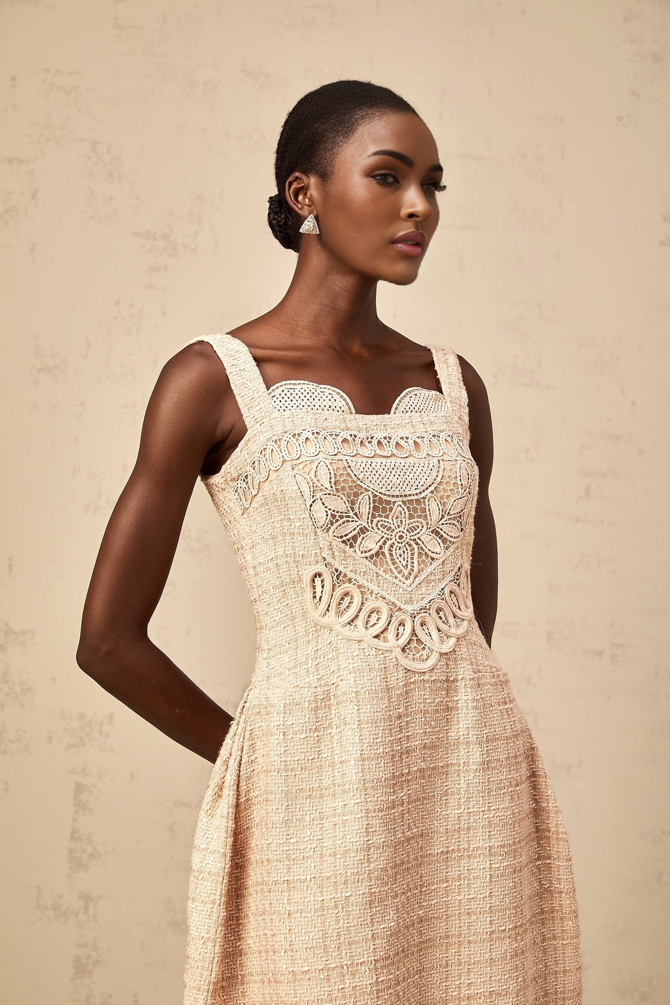 Woman wearing short neutral colored dress with intricate embroidery pattern standing in relaxed pose