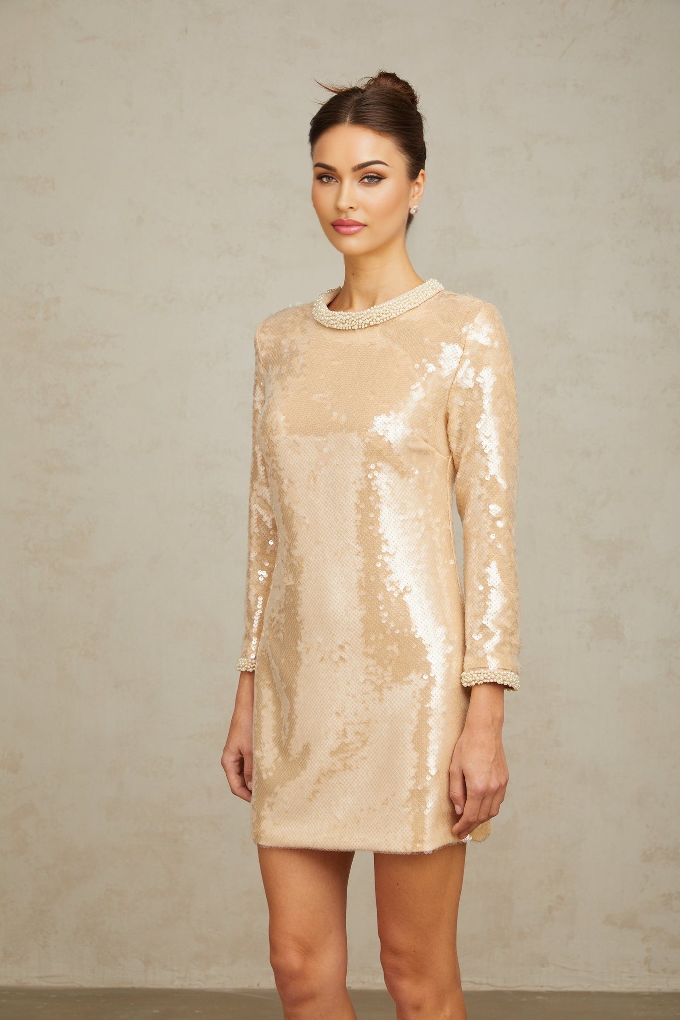 Woman wearing short neutralcolored dress with faux pearl and sequin embellishments