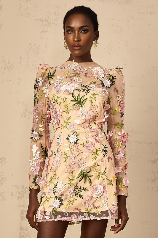 Woman wearing short pink dress with 3D floral applique details standing against plain background