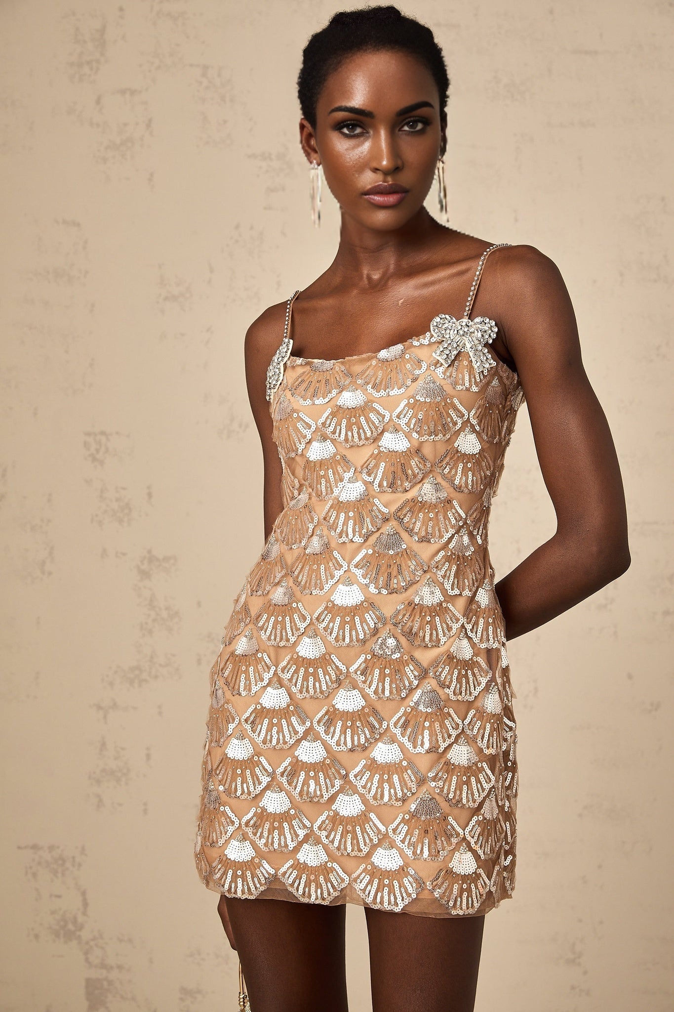 Woman wearing short sparkly gold dress with long sleeves and high neckline