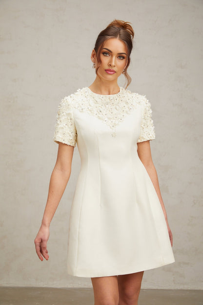 Woman wearing short white dress with colorful floral applique details and puff sleeves