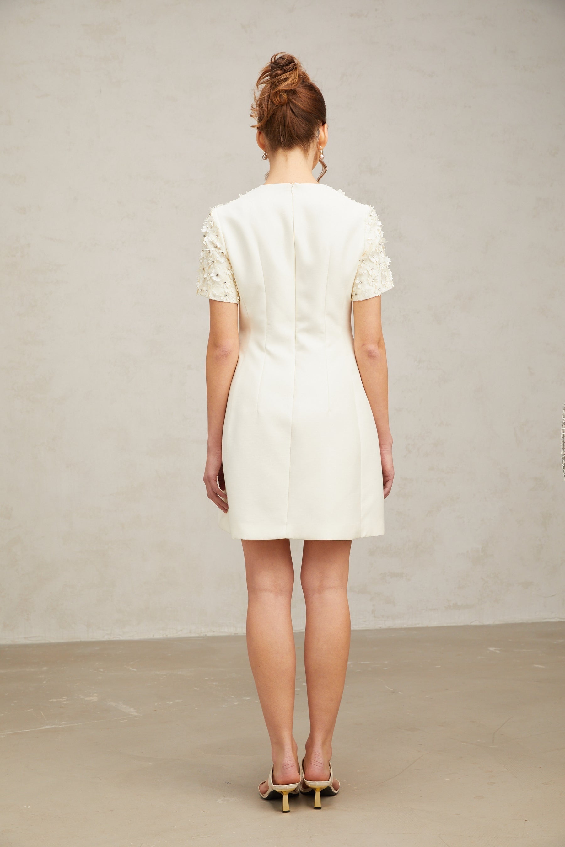 Woman wearing short white dress with colorful floral appliques scattered across fabric